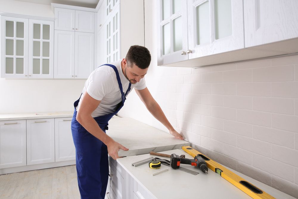 A worker helps to install a kitchen countertop in a white kitchen.