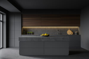 An interior shot of a black-tiled kitchen with a small island in the center. You can see a small fruit bowl on the island and several shakers on the counter behind it.