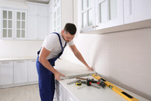 A worker helps to install a kitchen countertop in a white kitchen.