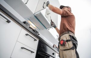A man uses a screwdriver to install new white kitchen cabinets