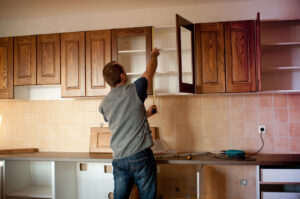 A contractor works to install new kitchen cabinets above a kitchen countertop