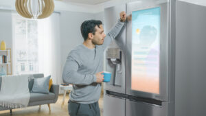 A man standing at his smart refrigerator with a giant touch screen on the door