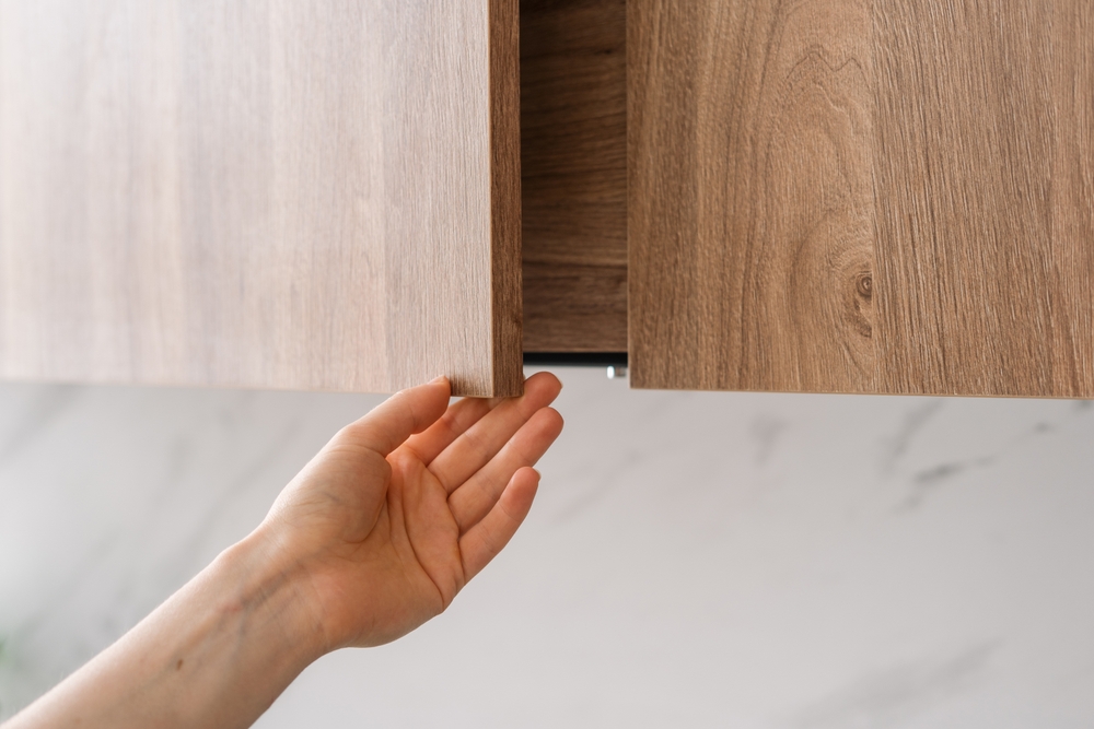 A woman opening a wooden kitchen cabinet
